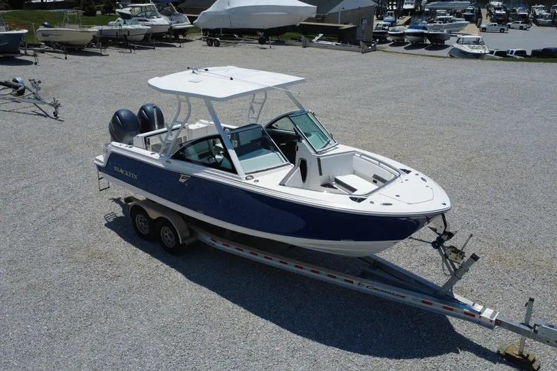 Slide: The Image of 2020 Blackfin 242 DC boat on trailer in a gravel lot, surrounded by other boats. - 6