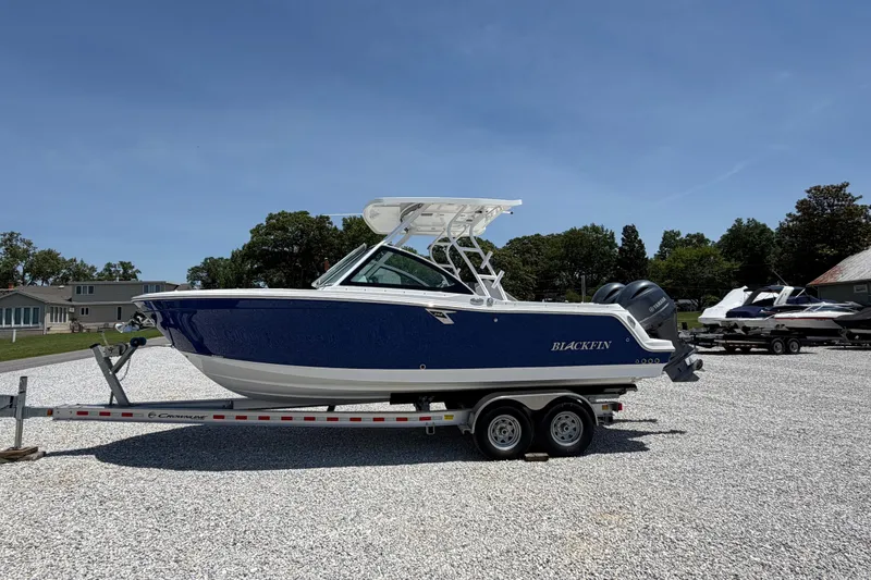 Slide: The Image of 2020 Blackfin 242 DC boat on trailer, blue and white design, parked outdoors. - 2