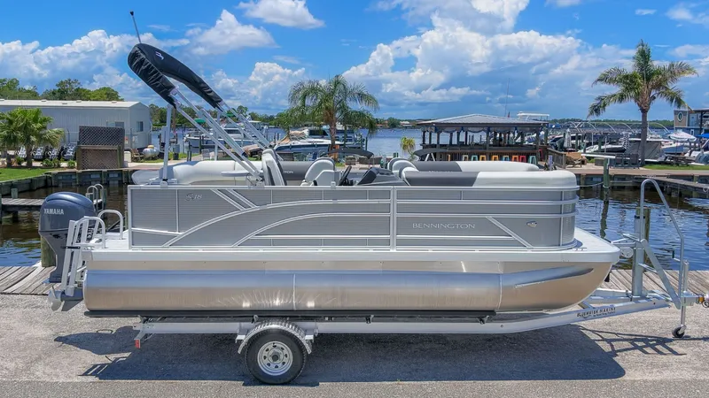 Slide: The Image of A 2027 Bennington 18 S CRUISE pontoon boat on a trailer, set against a scenic marina. - 23
