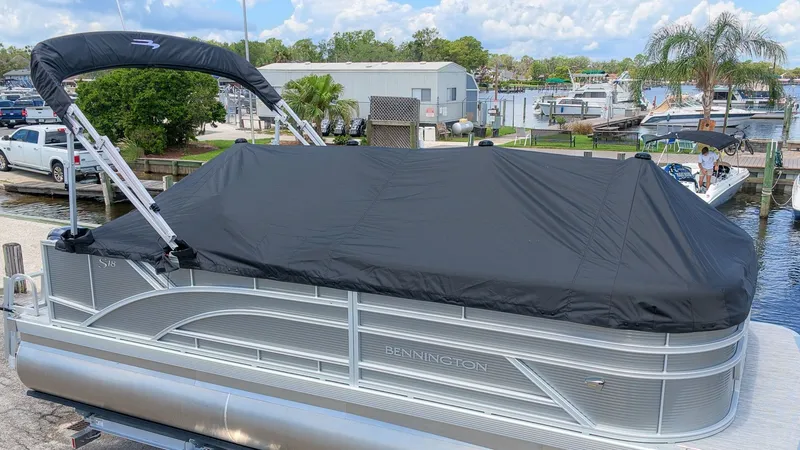 Slide: The Image of A Bennington 18 S Cruise pontoon boat with a black cover, parked at a marina with other boats. - 2
