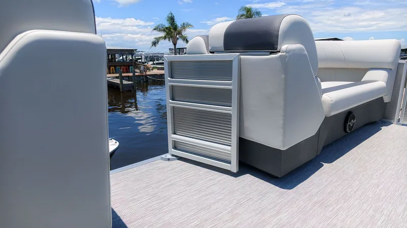 Slide: The Image of A modern pontoon boat with gray and white seating, on calm waters with palm trees in the background. - 11