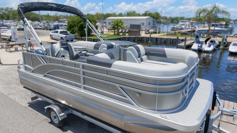 Slide: The Image of A modern pontoon boat with gray upholstery and a black sunshade, parked on a trailer by the water. - 23