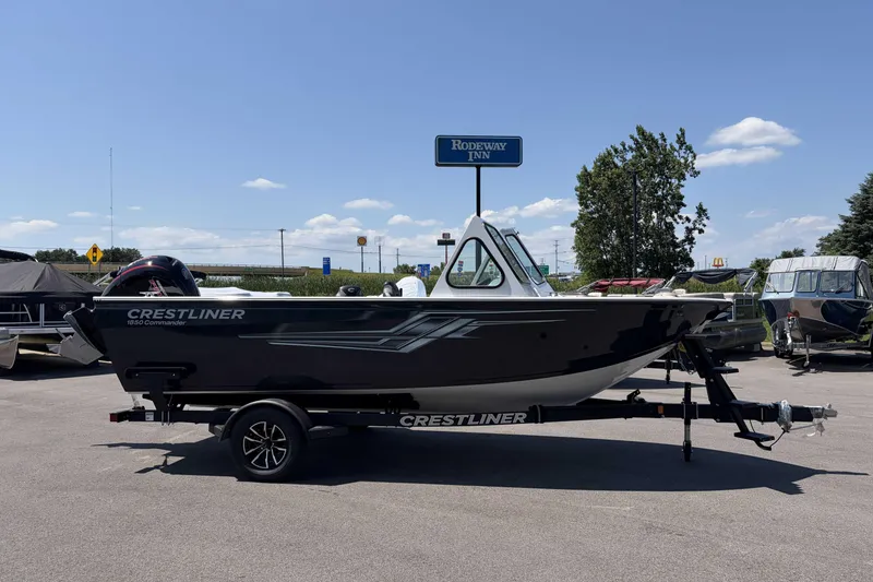 Slide: The Image of 2027 Crestliner 1850 Commander boat on trailer in parking lot, clear sky background. - 2