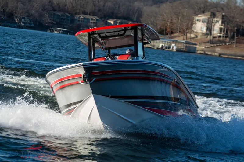 Slide: The Image of A 2023 Fountain 32 NX boat speeds across the water, featuring red accents and a T-top. - 4