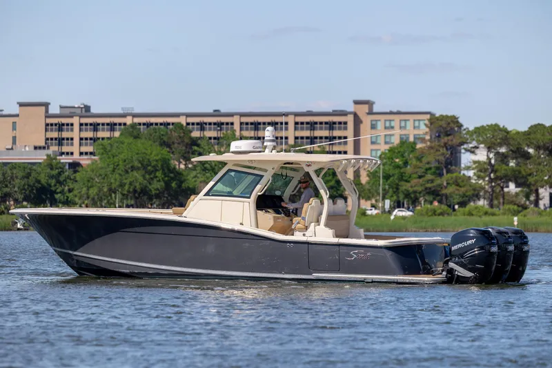 Slide: The Image of 2019 Scout 355 LXF boat cruising on a calm river with modern buildings in the background. - 5