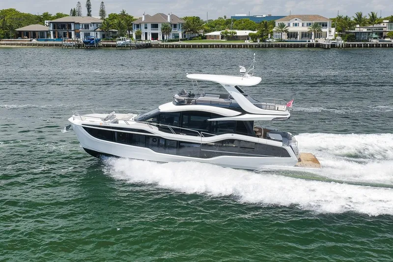 The Image of 2022 Galeon 560 Fly yacht cruising on water near luxury waterfront homes. - 1
