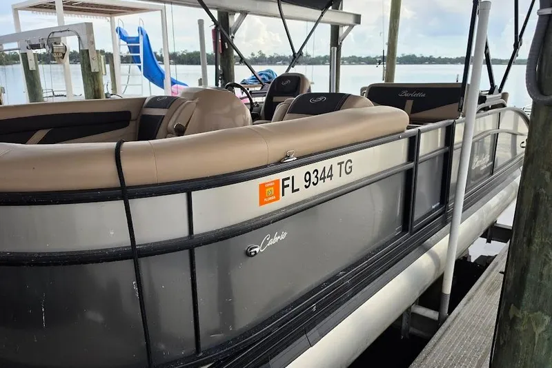 Slide: The Image of 2022 Barletta Cabrio 24UE pontoon boat docked, featuring beige seating and Florida registration. - 5