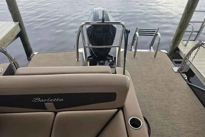 Slide: The Image of 2022 Barletta Cabrio 24UE pontoon boat with motor, docked on calm water. - 24