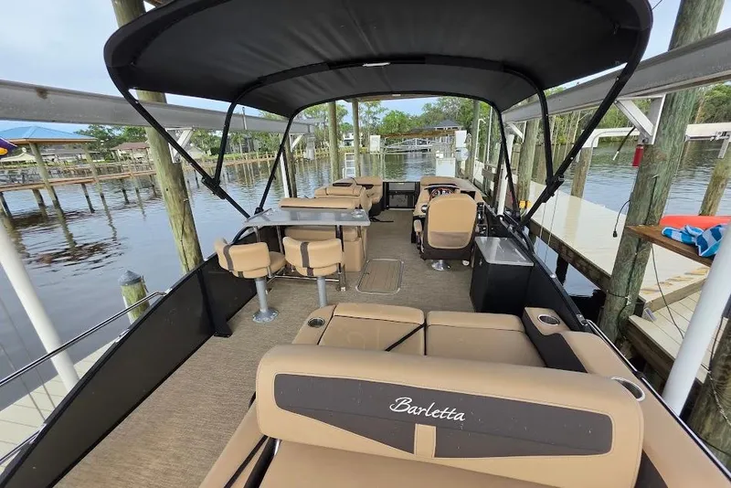 Slide: The Image of 2022 Barletta Cabrio 24UE pontoon boat with spacious seating and canopy, docked by the water. - 9
