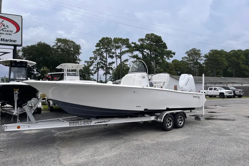 Slide: The Image of 2027 Tidewater 2500 Carolina Bay boat on trailer at dealership, surrounded by trees and vehicles. - 1
