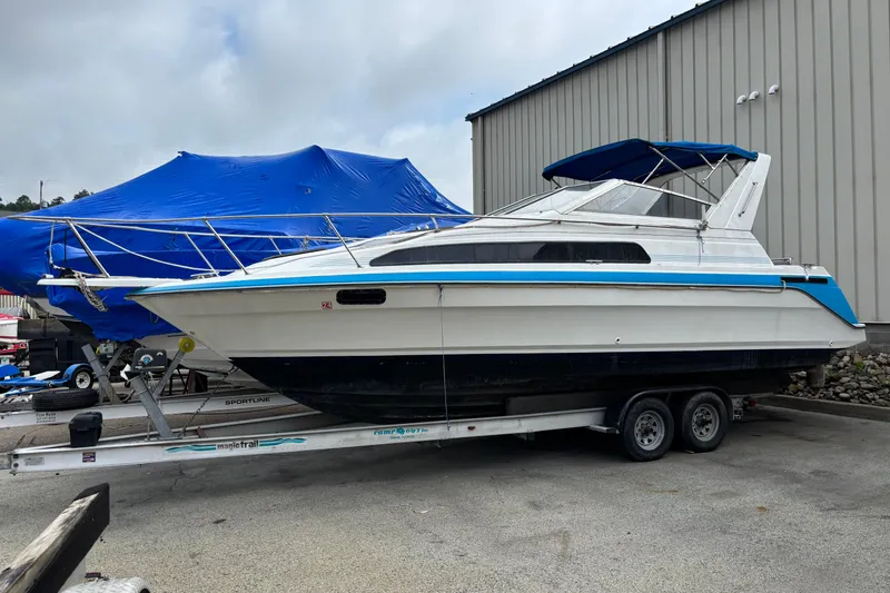 Slide: The Image of 1992 Bayliner 2850 Contessa boat on trailer, parked near a building with blue cover. - 1