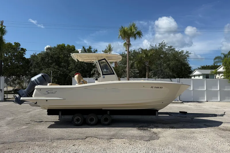 The Image of 2018 Scout 235 XSF boat on trailer, parked outdoors under clear blue sky. - 0
