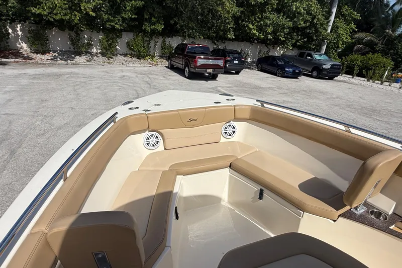 Slide: The Image of 2018 Scout 235 XSF boat with tan seating and speakers, parked near vehicles. - 11