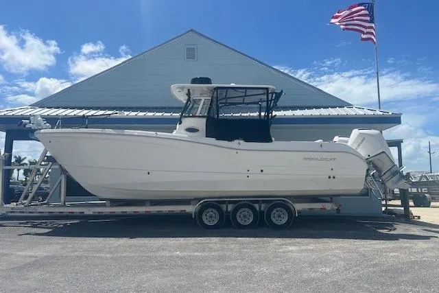 The Image of 2024 World Cat 295 CC boat on trailer, parked near a building with an American flag. - 1