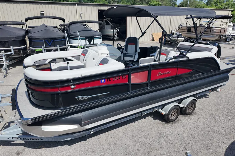 The Image of 2022 Barletta Corsa 23U pontoon boat on trailer, black and red design, parked outdoors. - 0