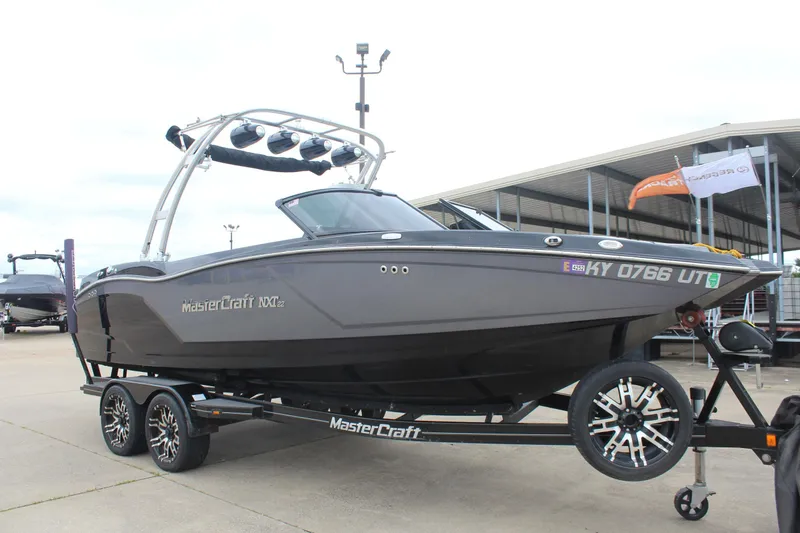 Slide: The Image of 2017 MasterCraft NXT22 boat on trailer, parked outdoors near a marina. - 2