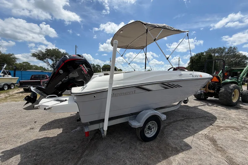 Slide: The Image of 2023 Bayliner Element E18 boat with canopy on trailer, parked outdoors under blue sky. - 4