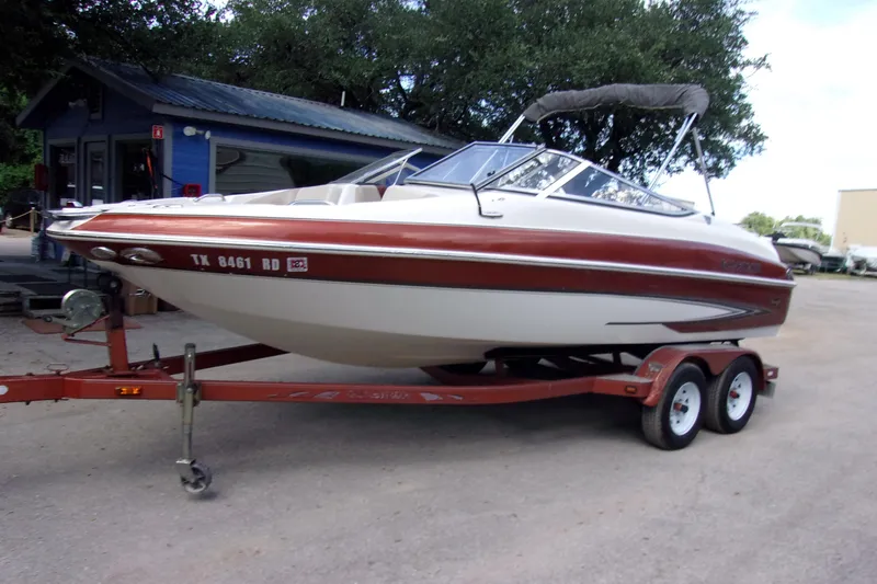 Slide: The Image of 2006 Glastron GXL 205 boat on trailer, parked outdoors near a blue building. - 2