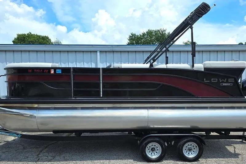 Slide: The Image of 2023 Lowe SS 210 pontoon boat on trailer, parked outdoors under a blue sky. - 15