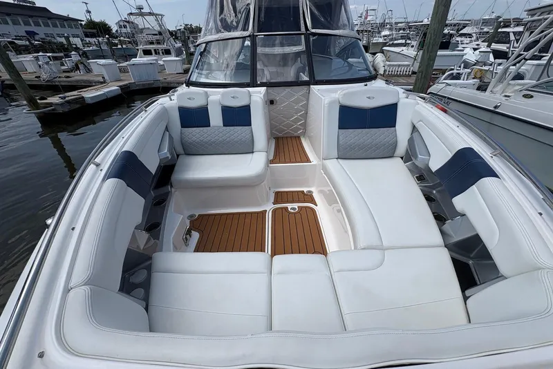 Slide: The Image of 2013 Chaparral 327 SSX boat interior with white seating and wood flooring at a marina. - 14