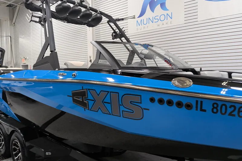 Slide: The Image of 2023 Axis A225 boat in showroom, blue and black design, Munson Surf Wake branding. - 13