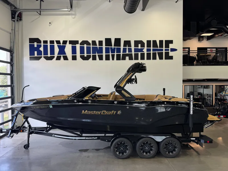 The Image of A black 2025 MasterCraft X24 boat on a trailer in a showroom. - 1