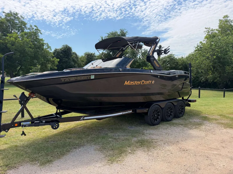 Slide: The Image of A 2025 MasterCraft X24 on a trailer in a grassy area with trees. - 2