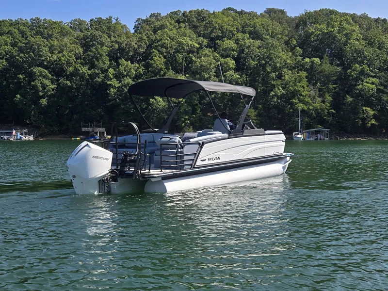 Slide: The Image of The image shows a 2027 Sylvan G-3 SLZ pontoon boat on a calm lake with a wooded shoreline. - 5