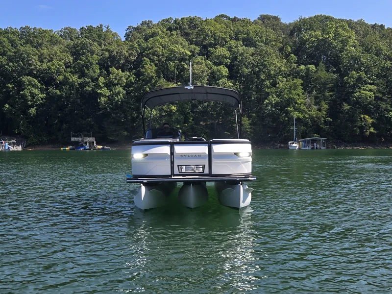 Slide: The Image of A 2027 Sylvan G-3 SLZ pontoon boat on a calm lake, surrounded by trees. - 2