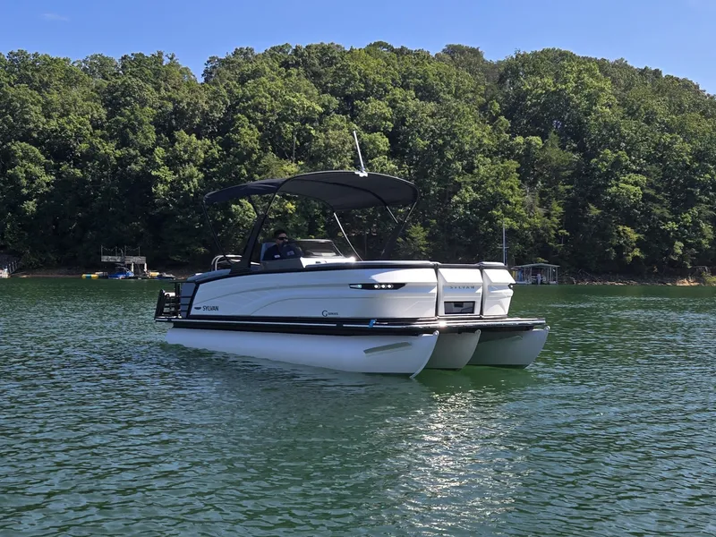 Slide: The Image of A 2027 Sylvan G-3 SLZ pontoon boat on a calm lake, surrounded by trees. - 3