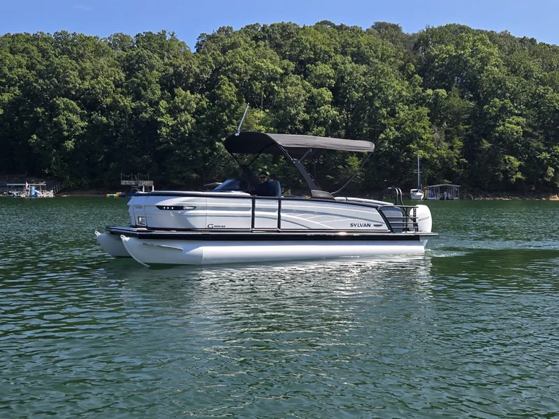 Slide: The Image of Sylvan G-3 SLZ 2027 pontoon boat on a calm lake with a wooded shoreline. - 41