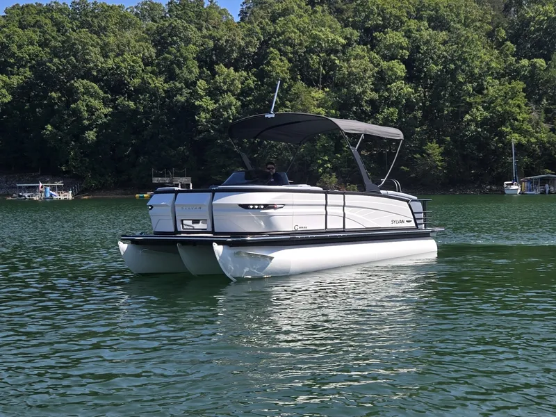 Slide: The Image of A 2027 Sylvan G-3 SLZ pontoon boat on a calm lake, surrounded by trees. - 1