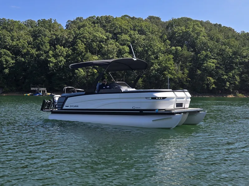 Slide: The Image of A 2027 Sylvan G-3 SLZ pontoon boat on a calm lake, surrounded by trees. - 38
