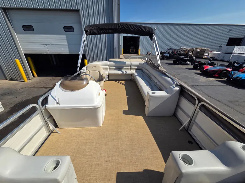 Slide: The Image of A spacious pontoon boat with beige seating and a black canopy, parked outside a warehouse. - 16