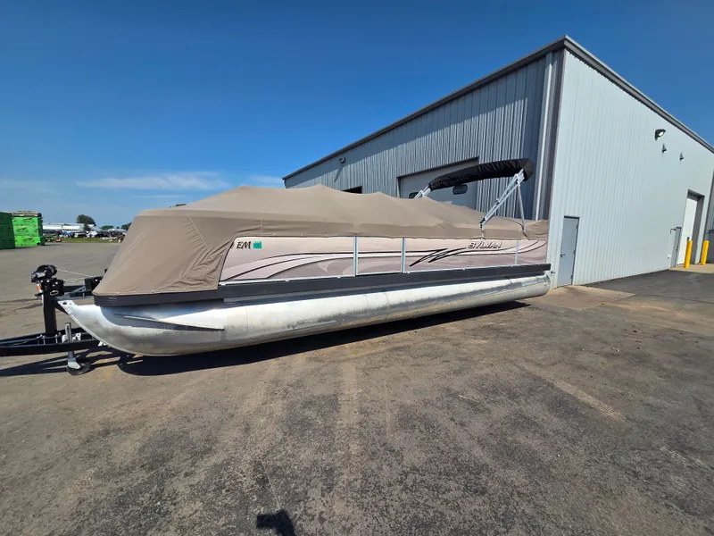 The Image of A 1998 Sylvan 826 Nexus pontoon boat is on a trailer outside a building. - 1