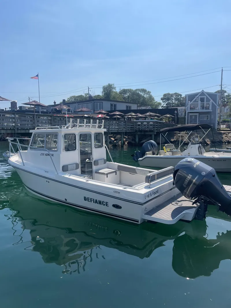 The Image of 2025 Defiance Admiral 220 EX docked, featuring an outboard motor and cabin, surrounded by other boats. - 0
