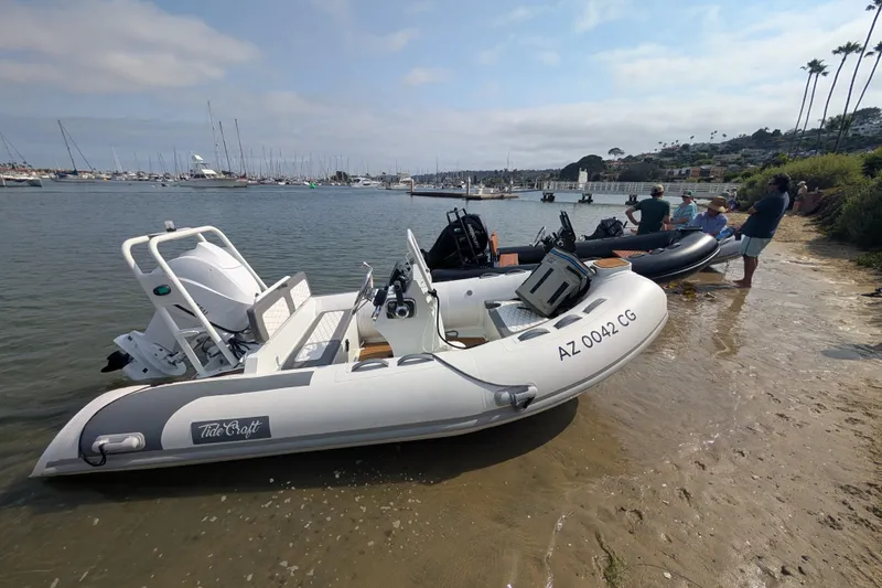 Slide: The Image of 2026 Tide Craft Nantucket 12 inflatable boat docked on a sandy shore with people nearby. - 8