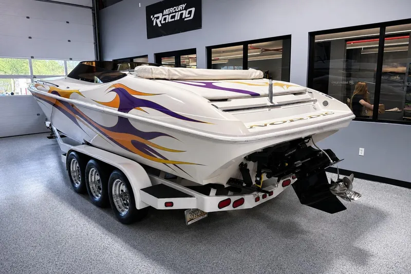 Slide: The Image of 2002 Nordic Boats 28' Heat with vibrant flame graphics on a triple-axle trailer in a showroom. - 3