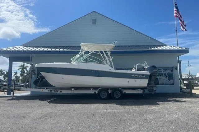 The Image of 2019 World Cat 230 DC boat on trailer, parked outside a building with an American flag. - 1