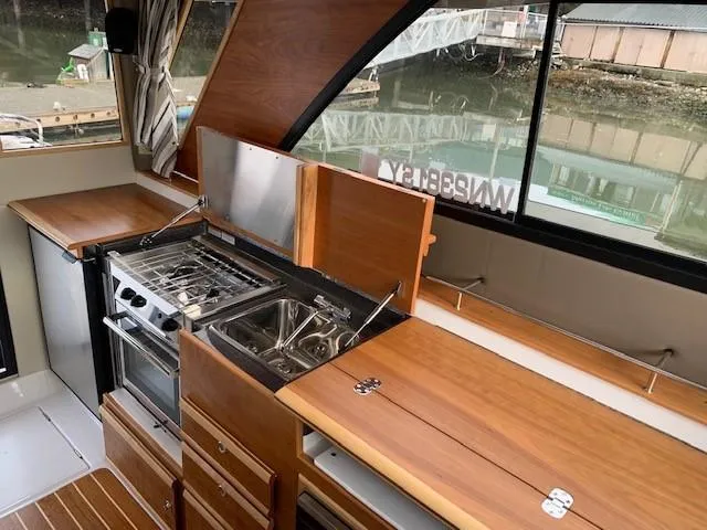Slide: The Image of Interior view of a modern boat kitchen with wooden cabinets, stove, and sink, surrounded by large windows. - 17