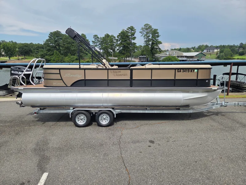 The Image of A 2024 Bentley Pontoons Legacy Navigator 243 on a trailer, featuring a Suzuki outboard motor. - 0