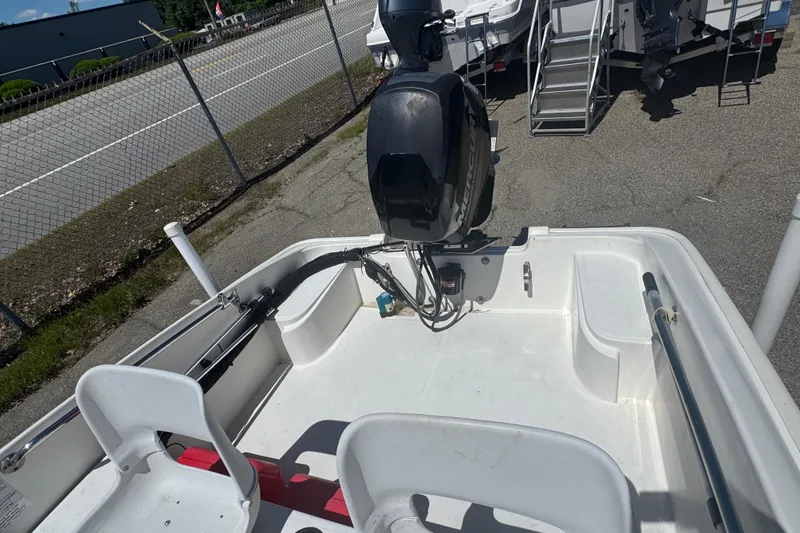 Slide: The Image of 2014 Boston Whaler 150 Super Sport boat interior with motor, parked near a fence. - 7
