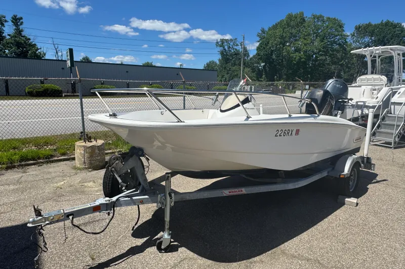 The Image of 2014 Boston Whaler 150 Super Sport boat on trailer, parked outdoors under clear sky. - 1