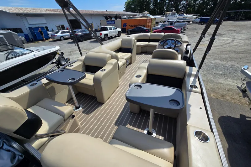 Slide: The Image of 2016 Manitou 23 Oasis SR pontoon boat with beige seating and tables, parked outdoors. - 13