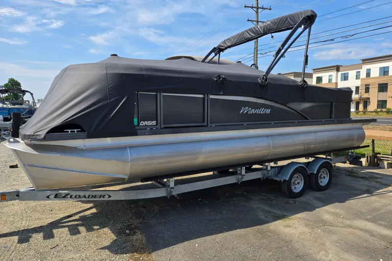 The Image of 2016 Manitou 23 Oasis SR pontoon boat on trailer, covered and parked outdoors. - 0