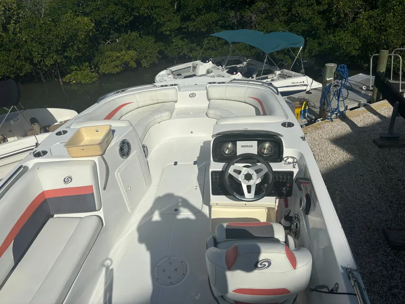 Slide: The Image of The image shows a 2021 Hurricane 188 SunDeck Sport -OB boat. It features white upholstery with red accents and a modern helm. Trees and another boat are visible in the background. - 7