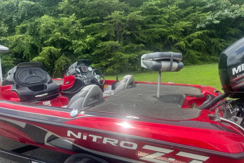 Slide: The Image of 2013 Nitro Z-6 boat with red exterior, featuring a Mercury engine, parked near lush greenery. - 2
