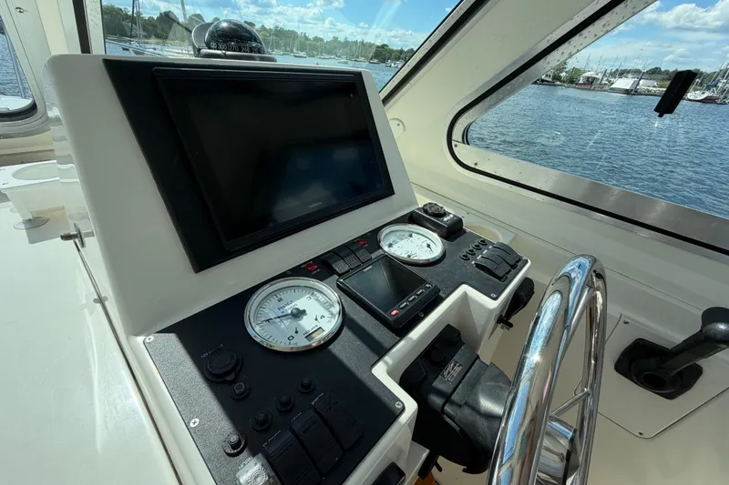 Slide: The Image of 2004 Back Cove 29 helm with gauges, steering wheel, and navigation screen, overlooking marina. - 12