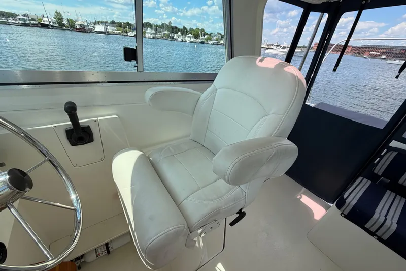 Slide: The Image of Captain's chair and helm inside a 2004 Back Cove 29 boat, overlooking marina. - 10