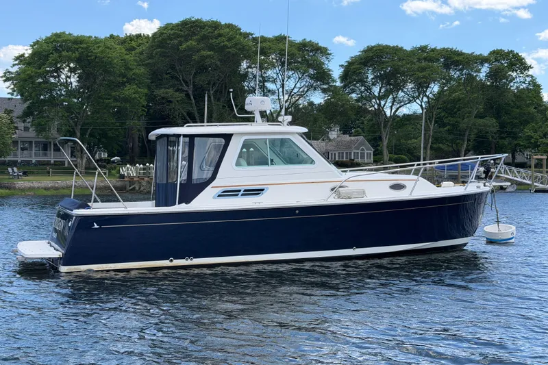 The Image of 2004 Back Cove 29 boat on calm water, surrounded by lush greenery and clear skies. - 0